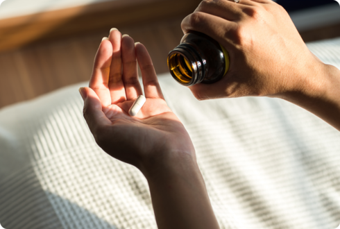 Zwei Hände: Die eine hält eine Medikamentendose, die andere eine Kapsel.