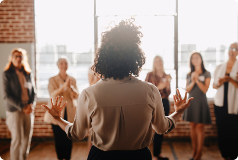 MS: Empowerment Eine Frau steht vor mehreren Personen und gestikuliert mit ihren Händen.