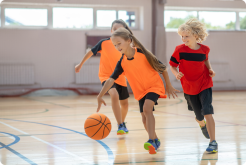 Drei Kinder spielen Basketball in einer Sporthalle. 