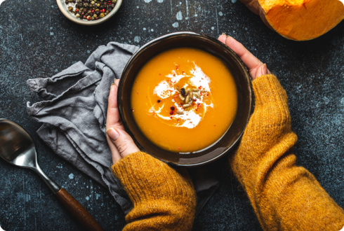 Die Hände einer Frau umfassen eine Schale mit Kürbissuppe. 