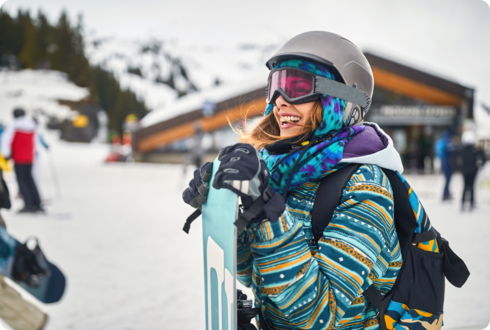 Eine Frau mit Skibrille und -helm hält ein Snowboard. 