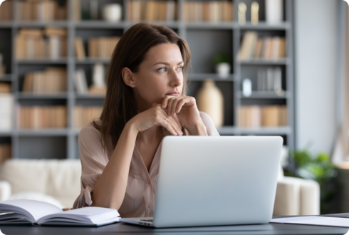 Eine Frau sitzt an einem Schreibtisch und schaut nachdenklich. 