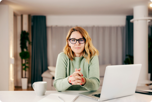 Eine Frau sitzt an einem Arbeitsplatz und hält die Hände verschränkt auf dem Tisch.