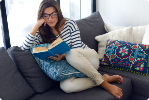 Eine Frau sitzt auf einem Sofa und liest ein Buch. 