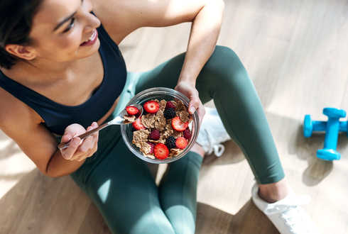 Eine Frau sitzt auf dem Boden und hält eine Schüssel mit Früchten in der Hand.