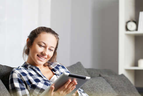 Eine junge Frau sitzt auf einem Sofa und schaut auf ein Tablet.