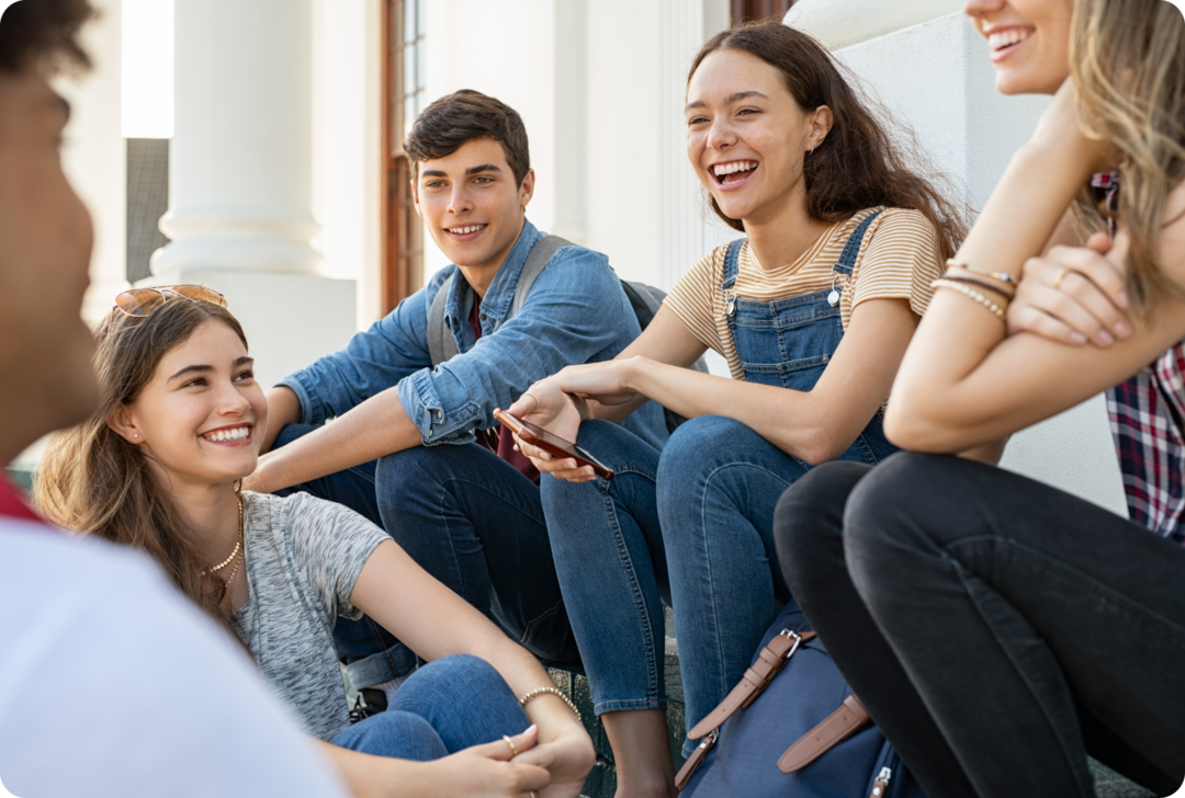 Jungendliche sitzen draußen und halten sich gut gelaunt.