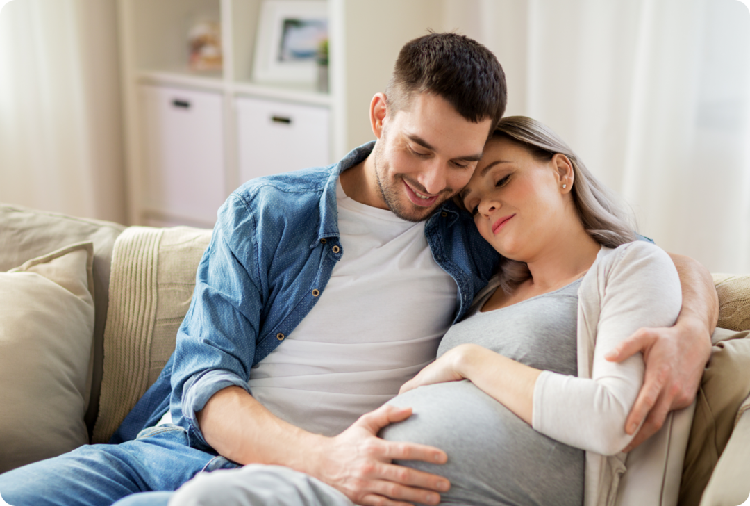 Eine schwangere Frau liegt im Arm eines Mannes.