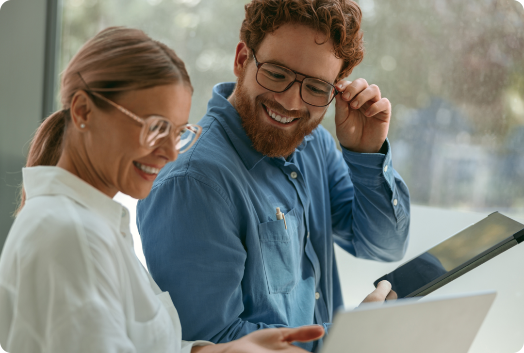 Eine Frau und ein Mann stehen nebeneinander und schauen auf zwei Tablets. 