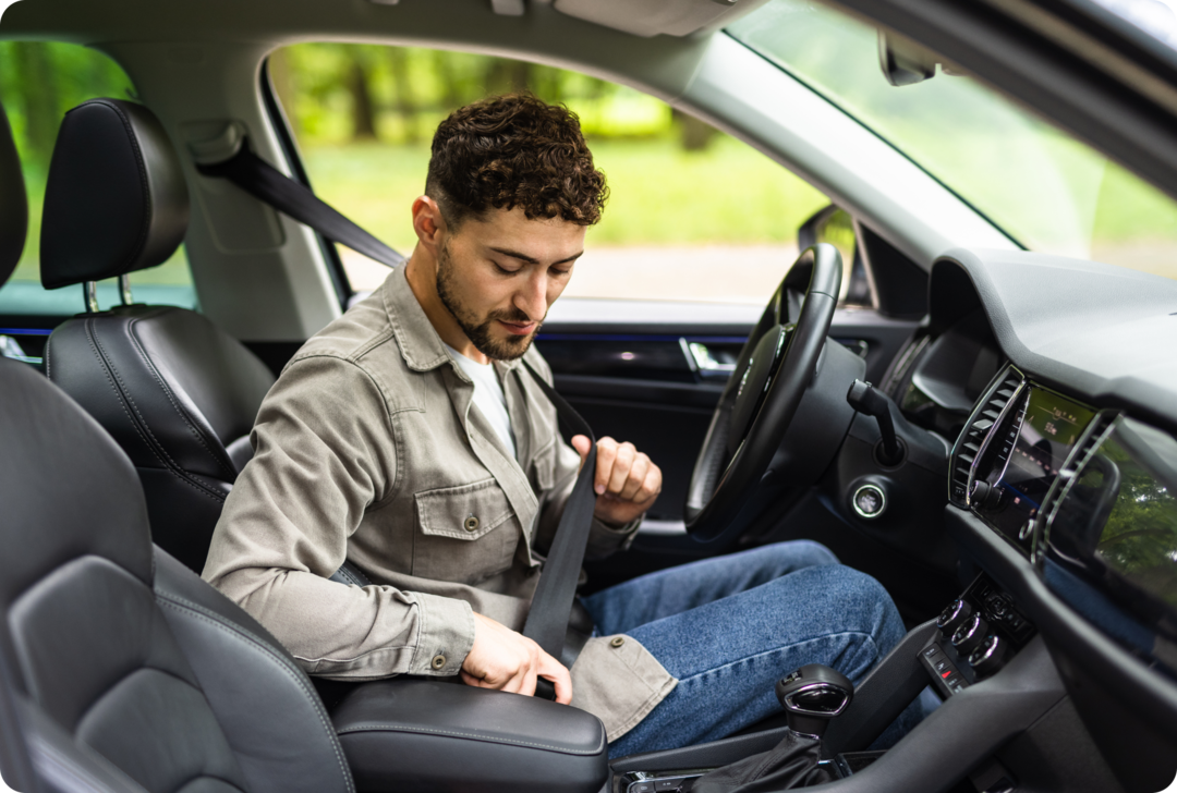 Ein junger Mann sitzt in einem Auto und legt den Sicherheitsgurt an. 