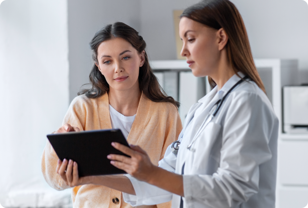 Eine Ärztin und eine Frau schauen auf einen Tablet-Computer.