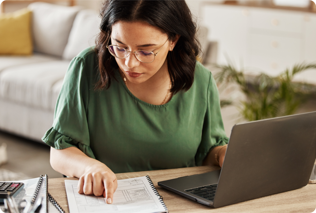 Eine Frau sitzt am Schreibtisch und schaut konzentriert auf ein Dokument. 