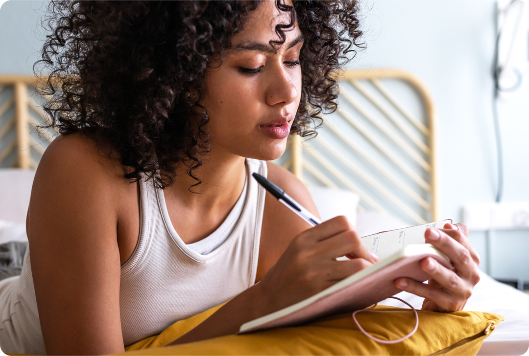 Eine Frau liegt auf einem Bett und macht sich Notizen in einem Kalender.