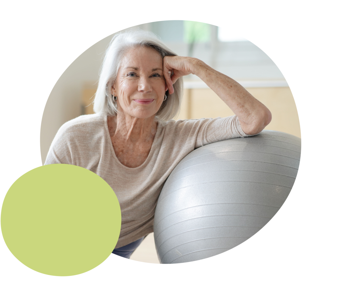 Eine ältere Frau lehnt sich an einen Gymnastikball.  