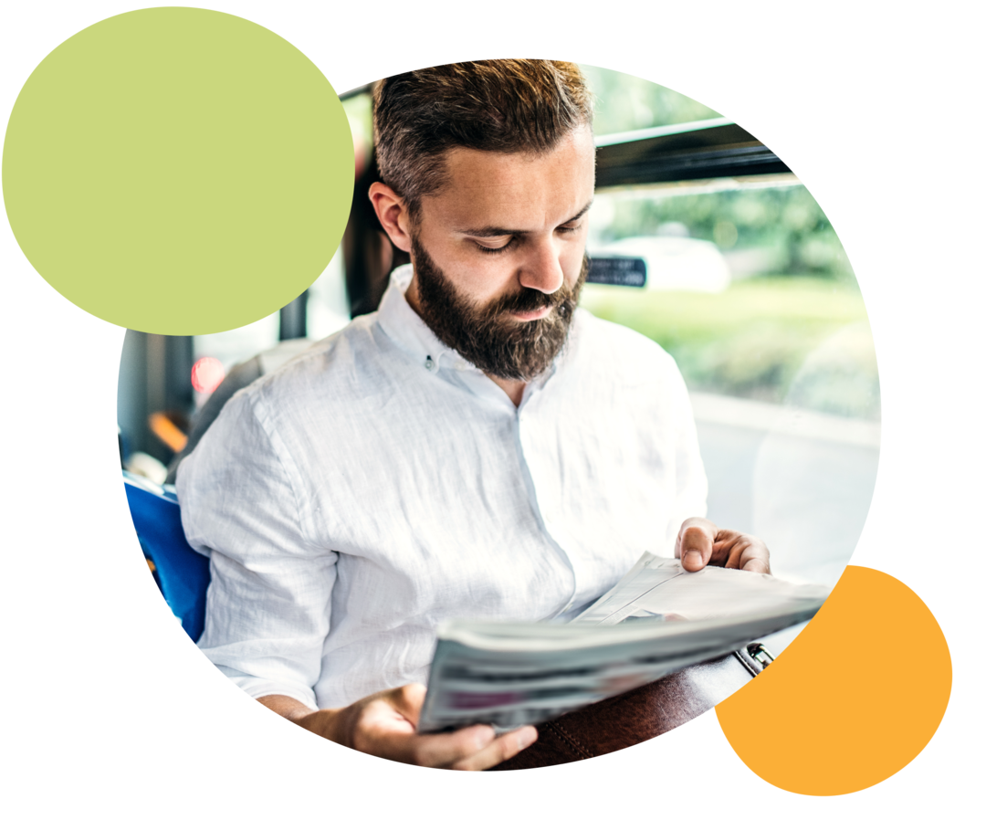 Ein Mann sitzt in einem Bus und liest eine Zeitung. 