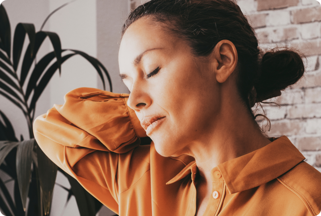 Eine Frau mit geschlossenen Augen hält ihren rechten Arm hinter ihren Nacken.