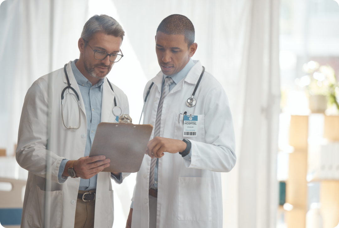 Zwei Männer mit weißen Kittel und Stethoskopen sprechen über einen Untersuchungsbericht.