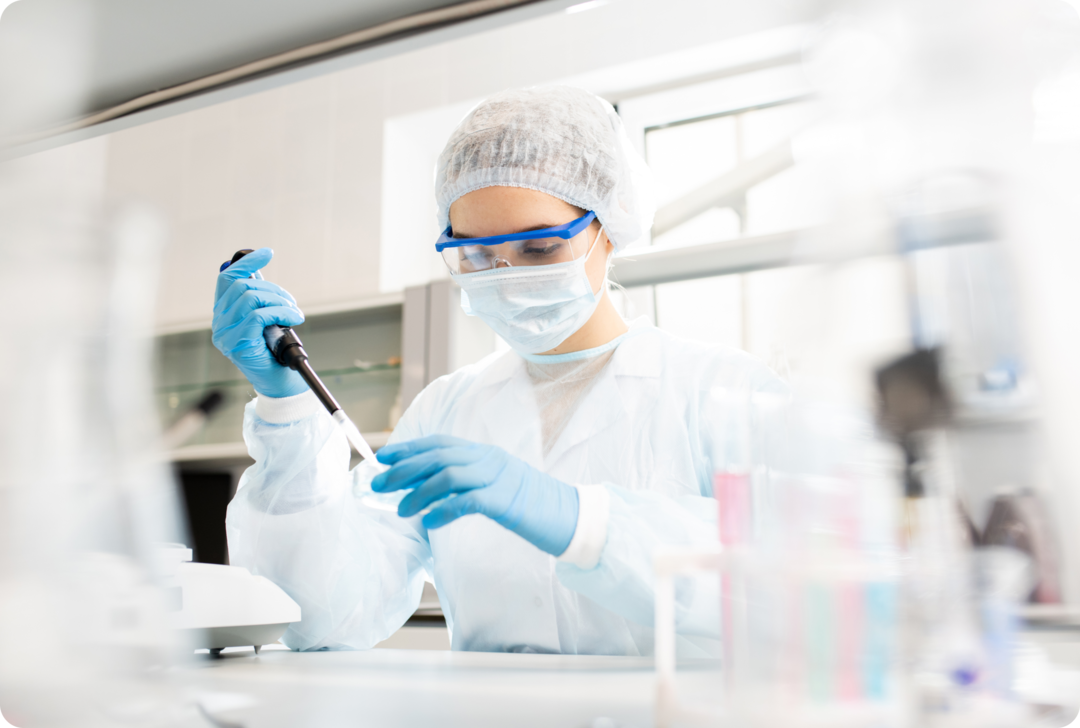 Eine Frau mit Mundschutz nimmt eine flüssige Probe mit einer Pipette.