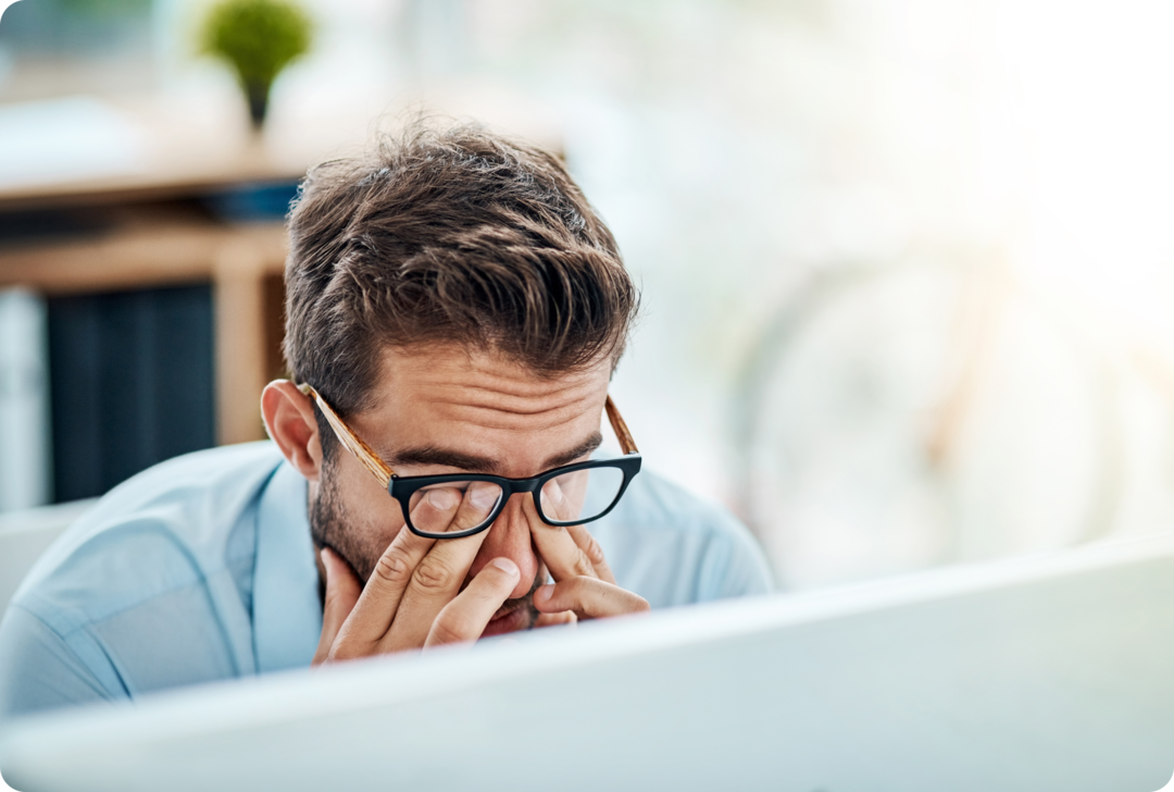 MS: kognitive Störungen Ein Mann sitzt vor einem Monitor und reibt sich seine Augen hinter seiner Brille.