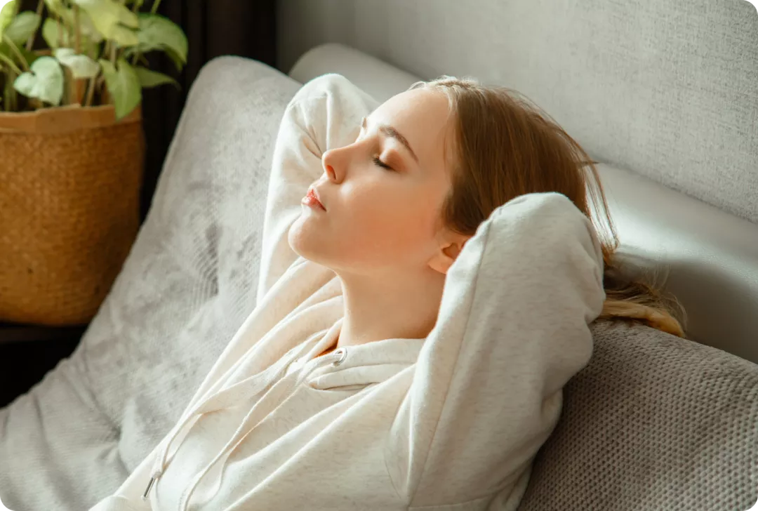 Atmung, Stimme und MS Eine junge Frau sitzt mit geschlossenen Augen auf einer Couch.