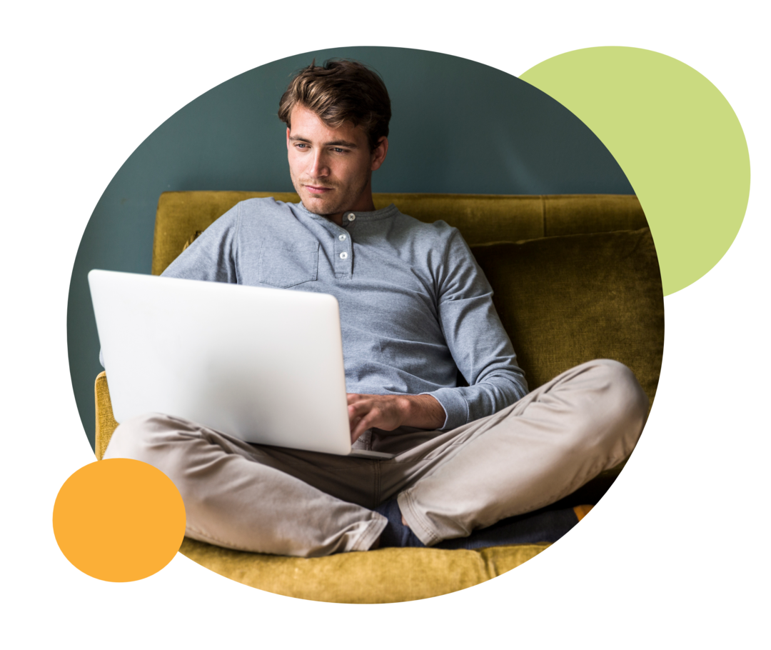 Ein Mann sitzt auf einer Couch und schaut auf ein Notebook